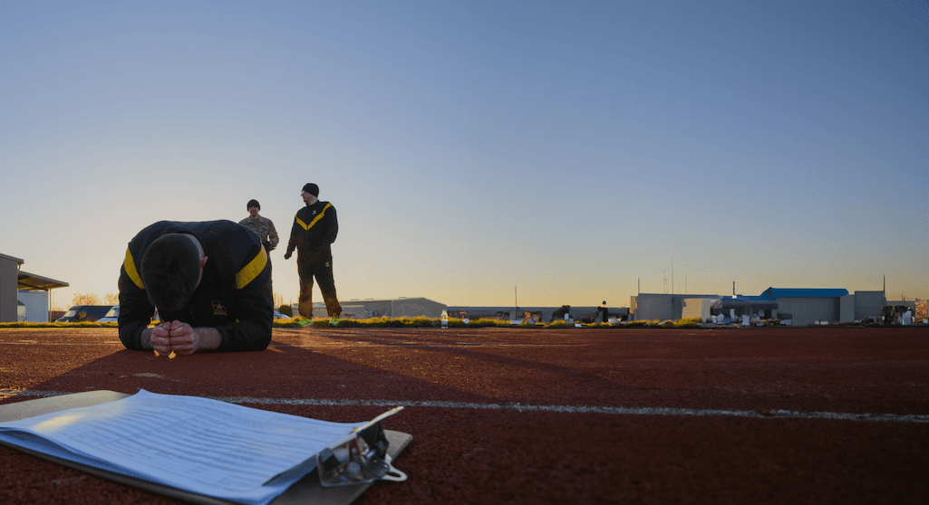 Soldier holds plank position during ACFT to assess core strength at dawn on track.