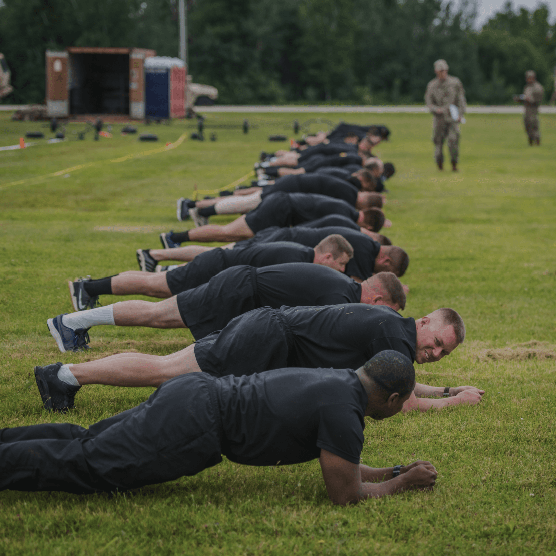 Line of soldiers holding the plank on a grassy field with test equipment nearby.